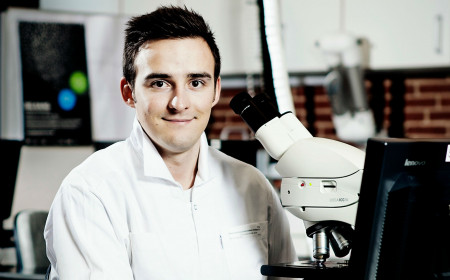 Bioanalytikerstuderende sidder ved mikroskop og smiler